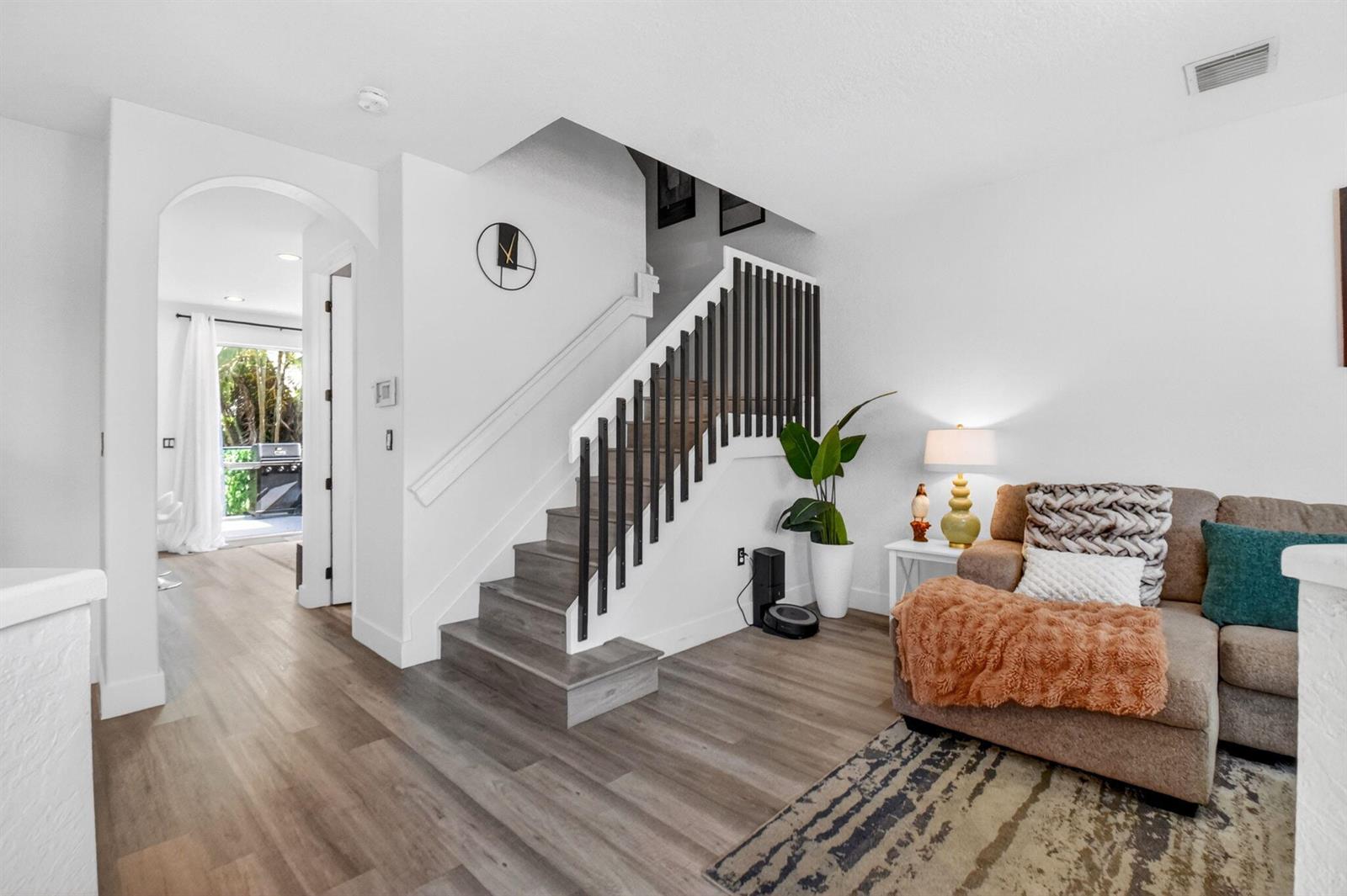 A living room features wood-look flooring, a staircase with dark railings, and a brown sofa — 173 Lake Monterey Circle, Boynton Beach FL 33426, BOYNTON BEACH, FL