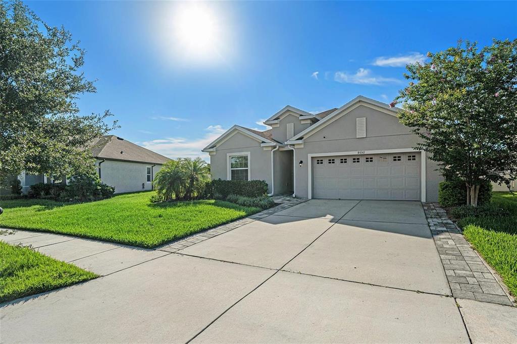 A single-story suburban house with a gray stucco exterior, a two-car garage, and a driveway — 8052 OLIVE BROOK DRIVE, WESLEY CHAPEL, FL