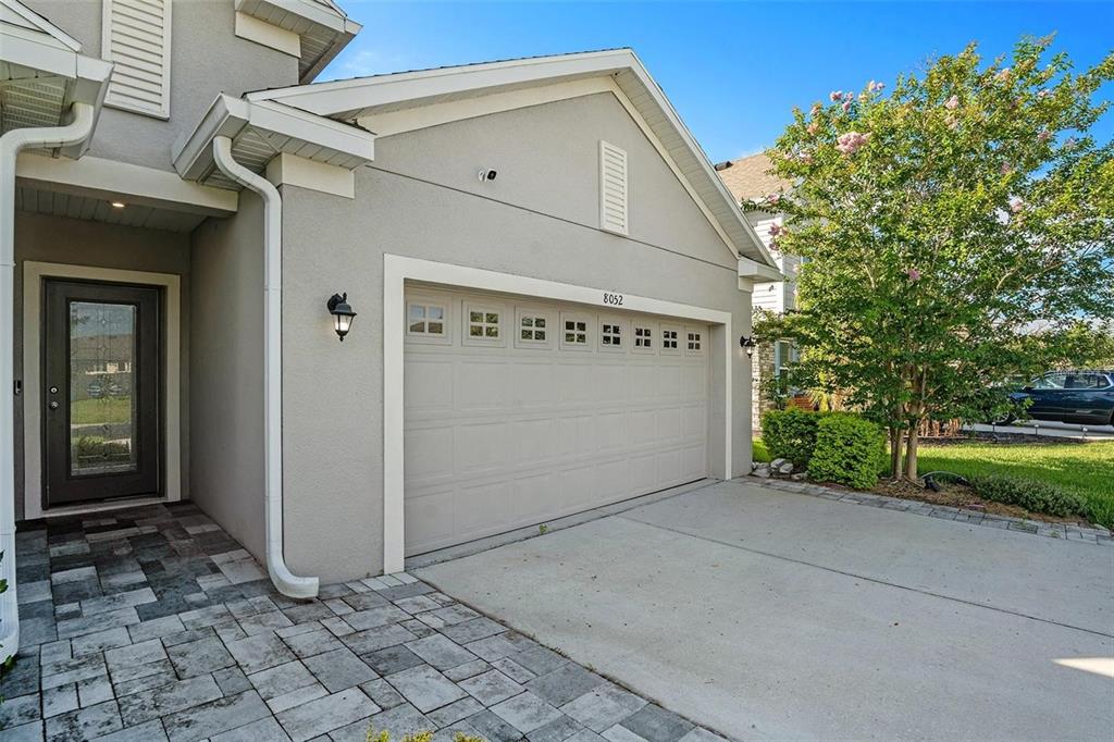 A gray house exterior features a two-car garage, a paved driveway, and a front entryway — 8052 OLIVE BROOK DRIVE, WESLEY CHAPEL, FL