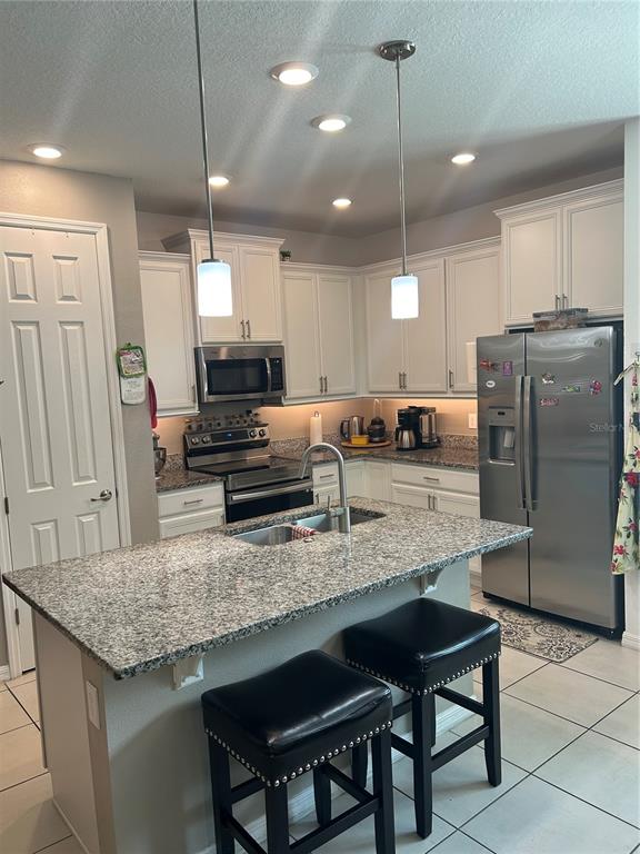 A kitchen features white cabinets, granite countertops, a center island with stools, and stainless appliances — 377 VESTRELLA DRIVE, KISSIMMEE, FL