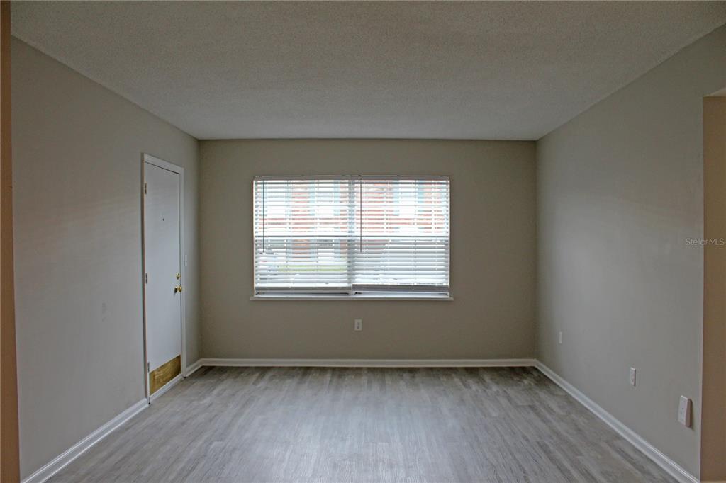 An empty room features light gray walls, wood-look flooring, and a single window with blinds — 1920 E EDGEWOOD DRIVE UNIT D9, LAKELAND, FL