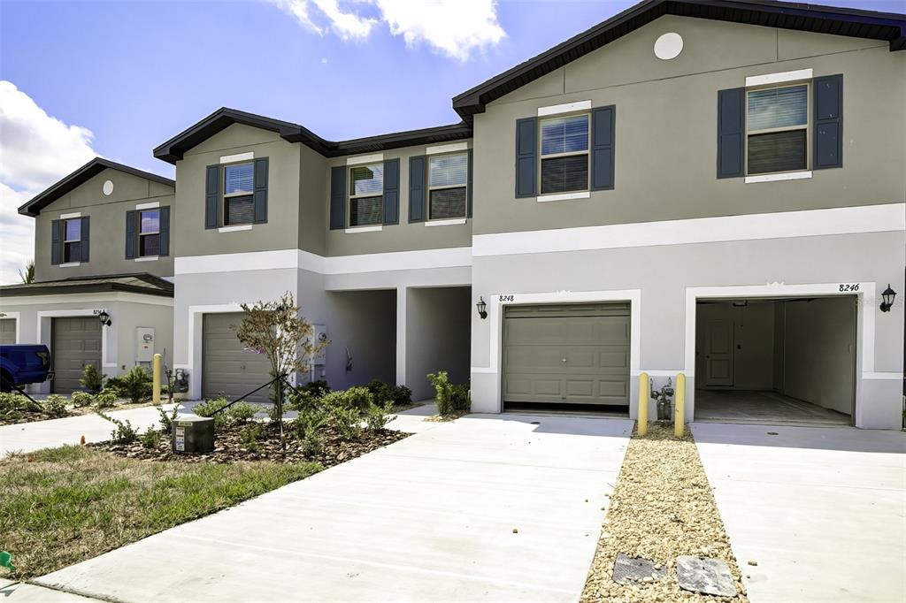 A row of two-story townhomes features gray stucco exteriors, dark shutters, and attached garages — 8248 CORNER PINE WAY, NEW PORT RICHEY, FL