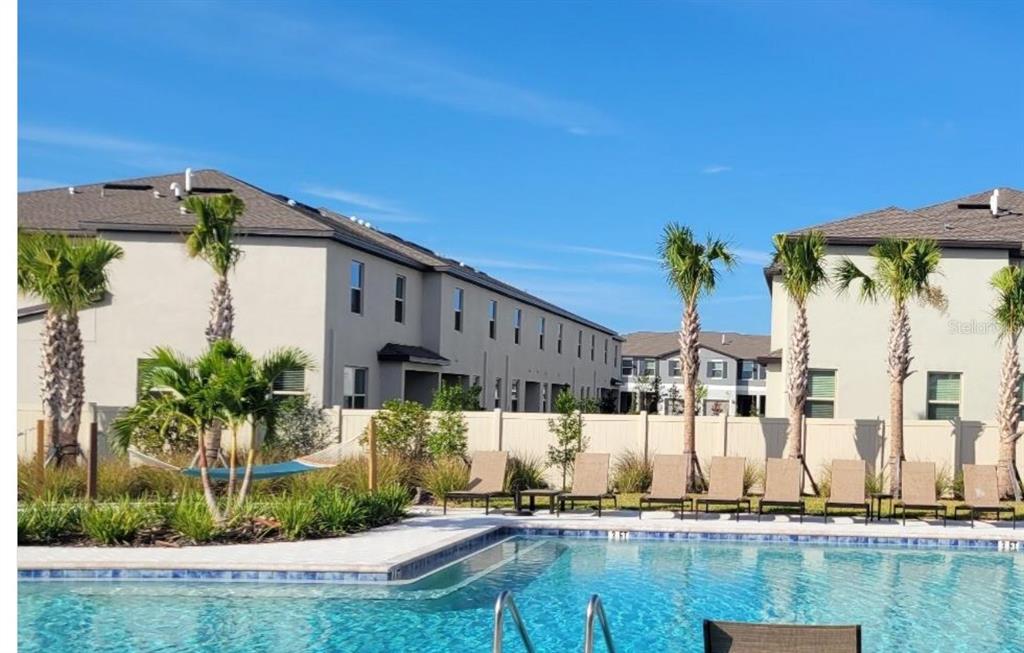 A swimming pool with lounge chairs and palm trees in front of multi-story apartment buildings — 8248 CORNER PINE WAY, NEW PORT RICHEY, FL