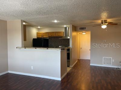 A kitchen with wooden cabinets and a breakfast bar overlooks a living area with flooring — 9105 W HILLSBOROUGH AVENUE UNIT I104, TAMPA, FL
