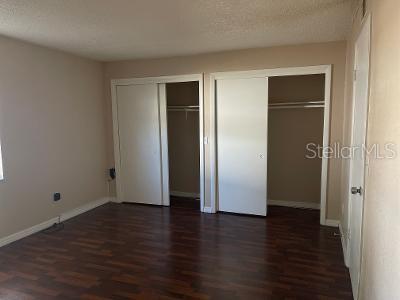 A bedroom with dark wood-look flooring, beige walls, and two white sliding-door closets — 9105 W HILLSBOROUGH AVENUE UNIT I104, TAMPA, FL