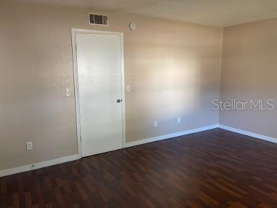 An empty room with beige walls, dark wood-look flooring, and a single white door — 9105 W HILLSBOROUGH AVENUE UNIT I104, TAMPA, FL