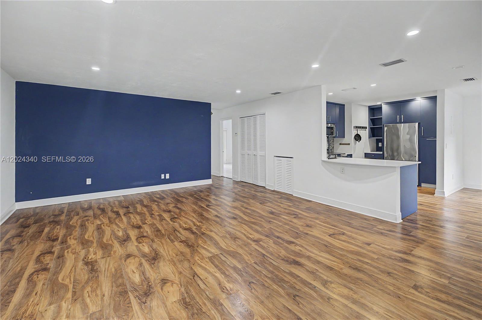 An open-concept living area features wood-look flooring, a blue accent wall, and a kitchen — 6815 Edgewater Dr # 201, Coral Gables FL 33133, CORAL GABLES, FL