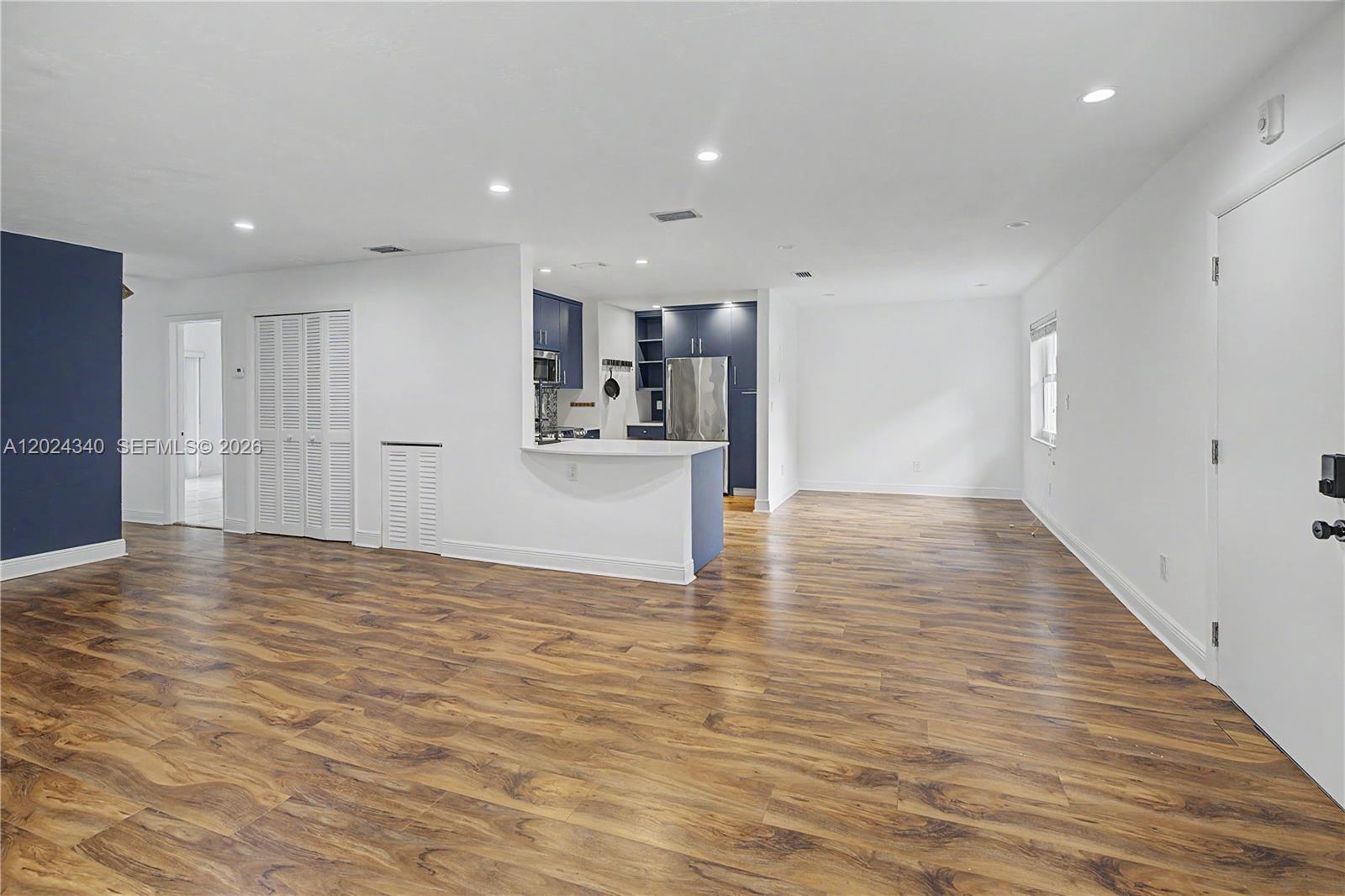 An open-concept living area features wood-look flooring, white walls, and a kitchen with blue cabinetry — 6815 Edgewater Dr # 201, Coral Gables FL 33133, CORAL GABLES, FL