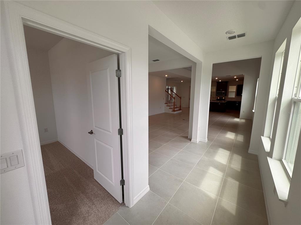 A hallway with tile flooring leads to an open living area with a staircase — 14727 FIELD DAISY DRIVE, WINTER GARDEN, FL