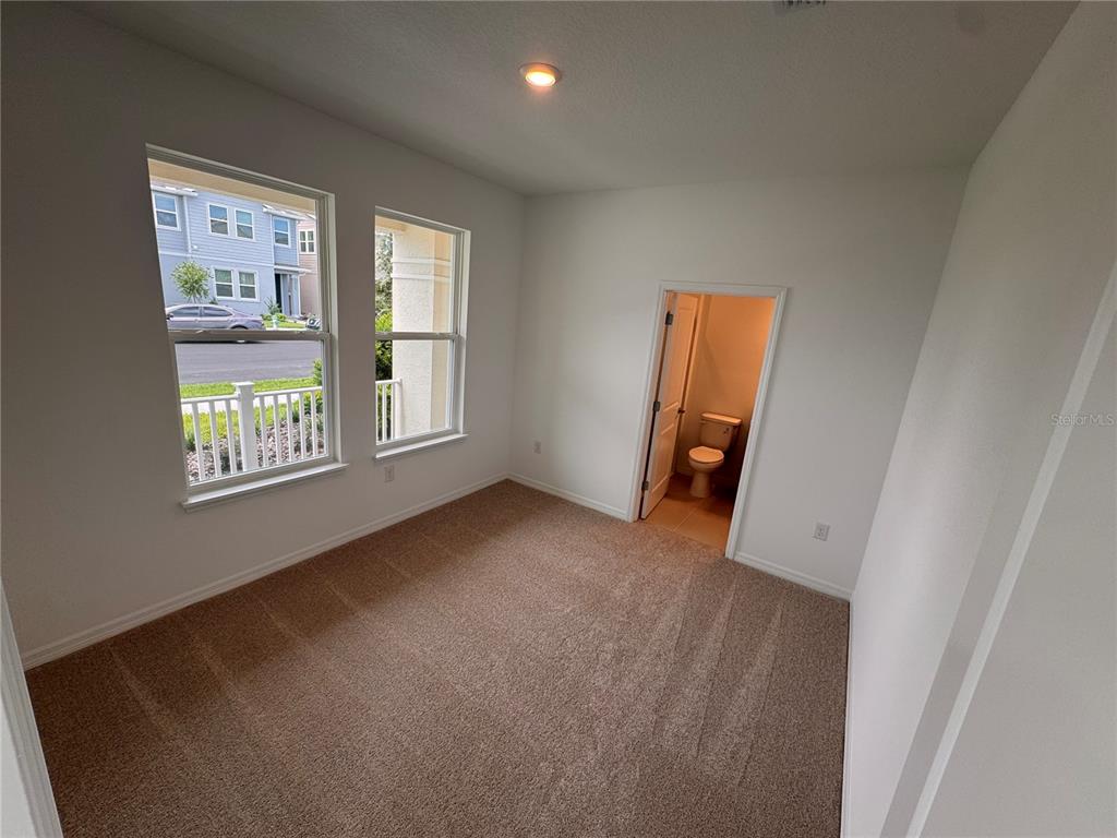 A carpeted room with two windows and an open doorway leading to a small bathroom — 14727 FIELD DAISY DRIVE, WINTER GARDEN, FL