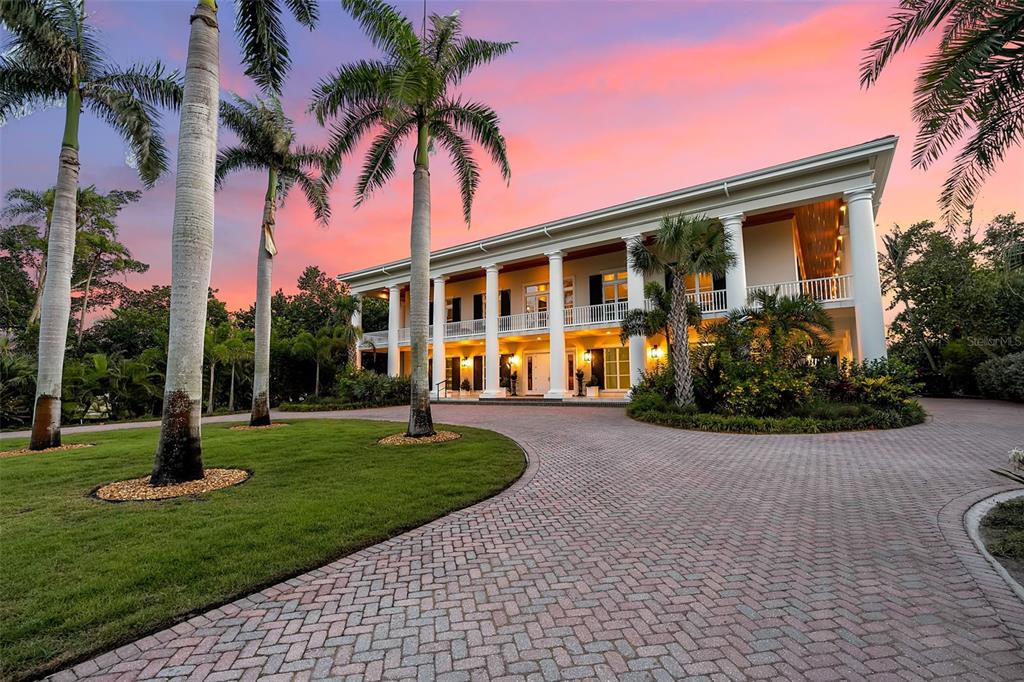 An aerial view of a large, two-story colonial-style house surrounded by palm trees at sunset — 8132 SANDERLING ROAD, SARASOTA, FL