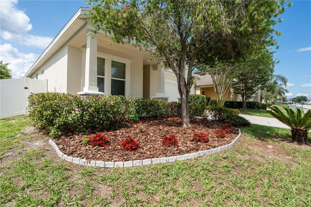 A single-story house exterior features a landscaped front garden with mulch, shrubs, and a tree — 1860 SKYVIEW DRIVE, AUBURNDALE, FL