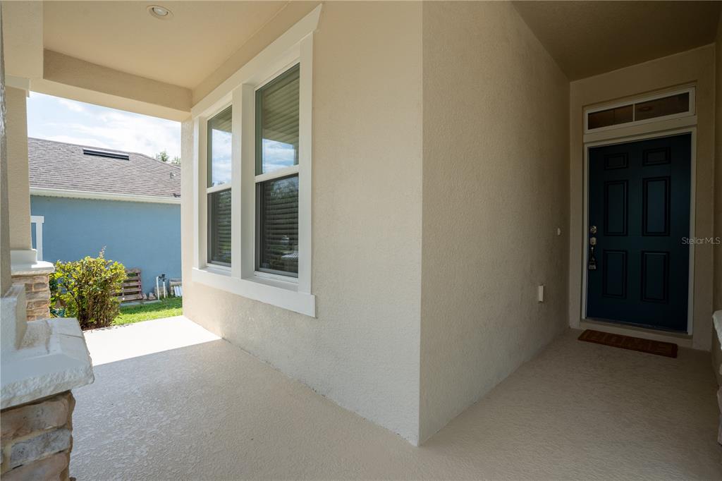 A covered front porch features a dark blue door, a large window, and light-colored stucco walls — 1860 SKYVIEW DRIVE, AUBURNDALE, FL