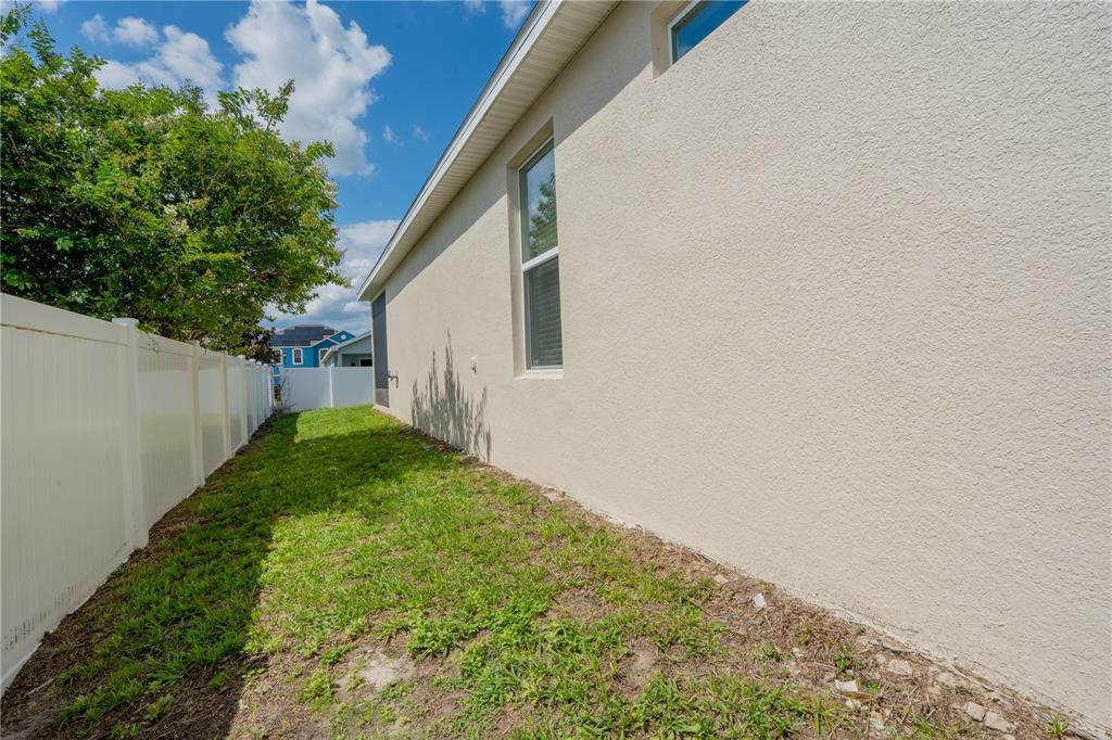 A narrow grassy side yard runs along the beige stucco exterior wall of a house — 1860 SKYVIEW DRIVE, AUBURNDALE, FL