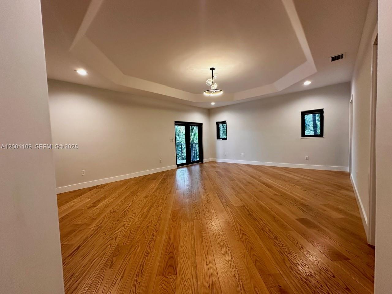 An empty room features a tray ceiling, hardwood floors, and glass doors leading outside — 223 NW 129th Ave # 0, Miami FL 33182, MIAMI, FL