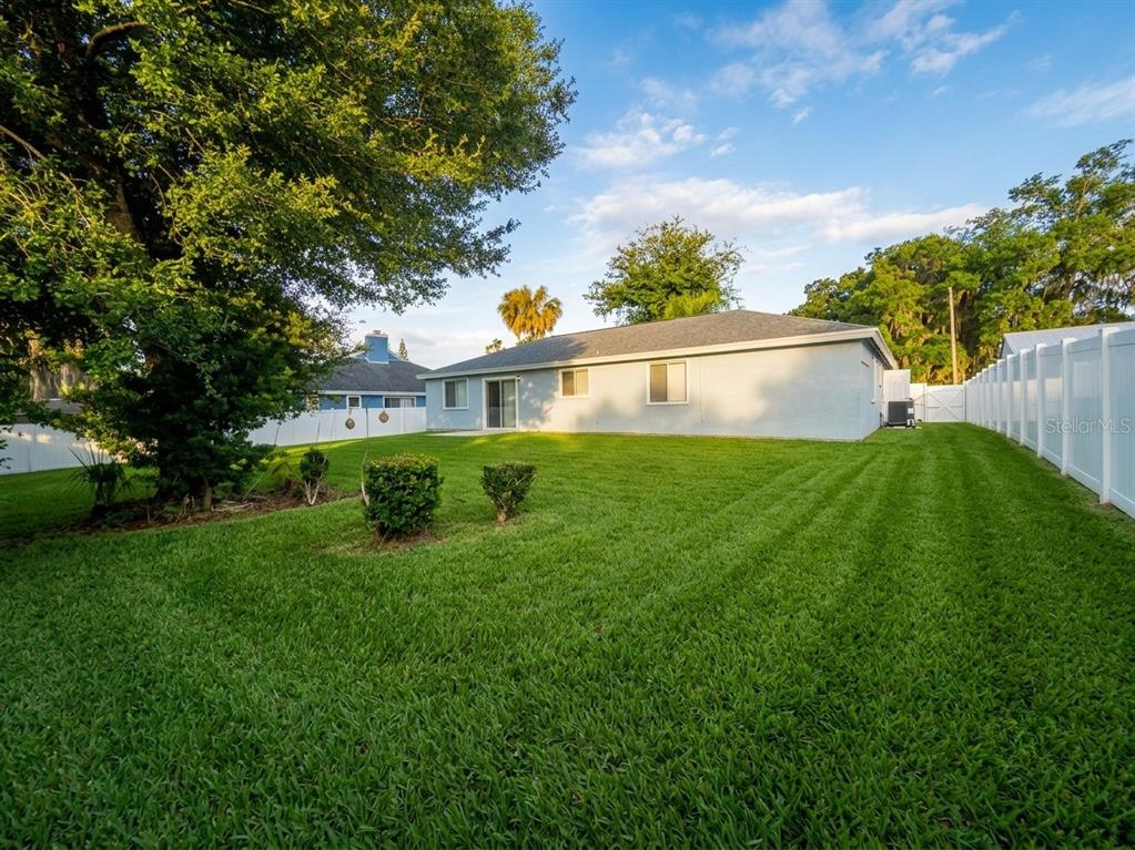 The backyard of a house features a green lawn, a white fence, and large trees — 1029 WINDSONG CIRCLE, APOPKA, FL