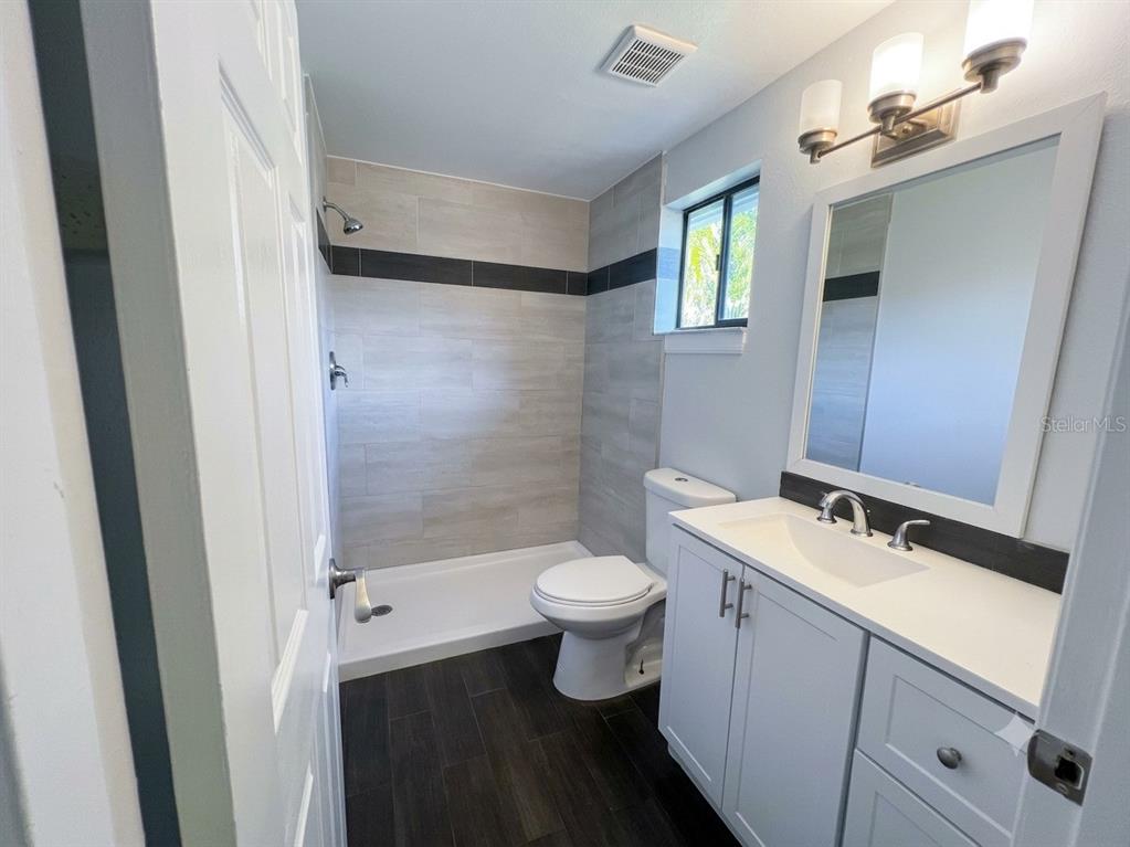 A bathroom features a white vanity, a toilet, and a walk-in shower with tiled walls — 1029 WINDSONG CIRCLE, APOPKA, FL