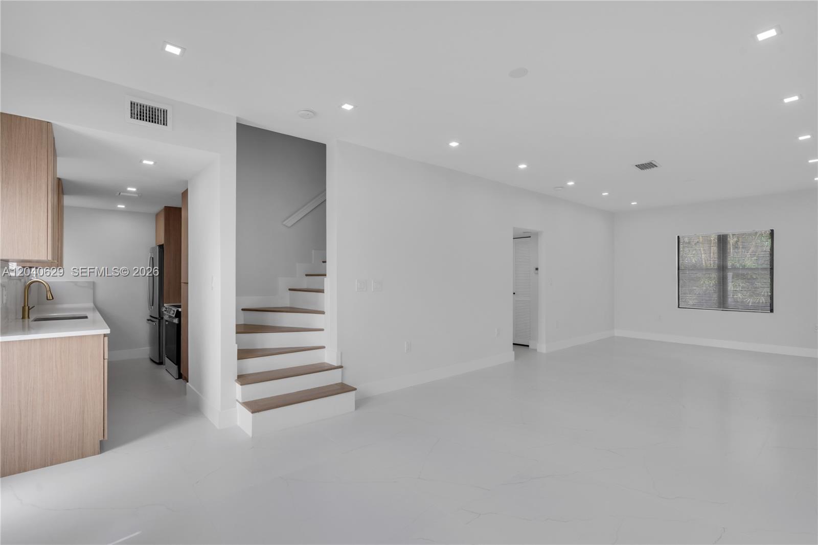 A modern, open-concept living area features white tile floors, recessed lighting, and a wooden staircase — 337 W 28th St, Miami Beach FL 33140, MIAMI BEACH, FL