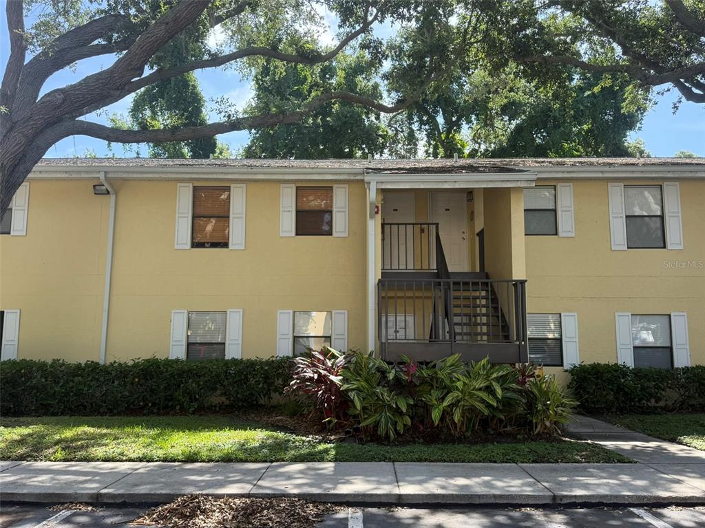A two-story yellow apartment building features a central staircase leading to upper-level entry doors — 3001 58TH AVENUE S UNIT 805, ST PETERSBURG, FL