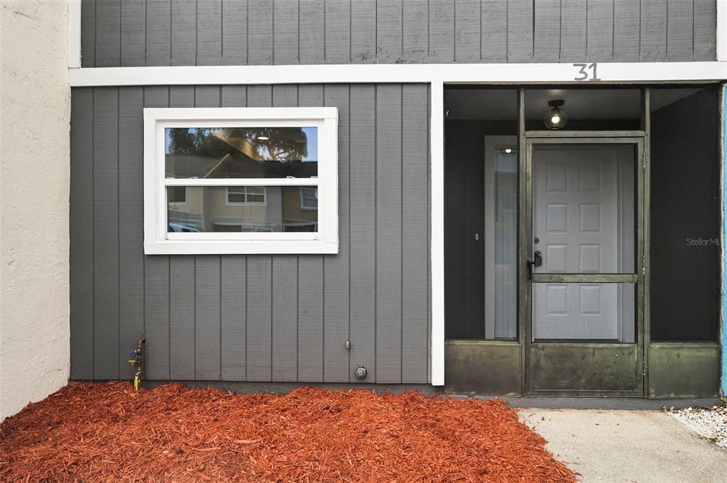 The exterior of a residential unit features gray vertical siding, a white-framed window, and a screened-in entryway — 2871 S PINES DRIVE UNIT 31, LARGO, FL