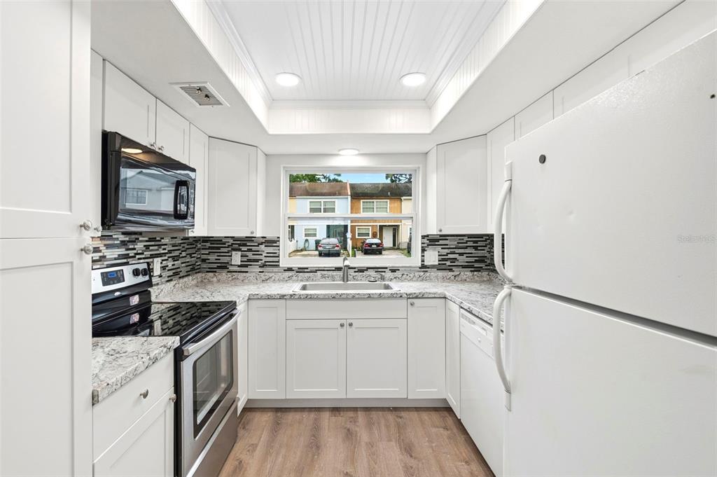 A white kitchen features granite countertops, a mosaic tile backsplash, and stainless steel appliances — 2871 S PINES DRIVE UNIT 31, LARGO, FL