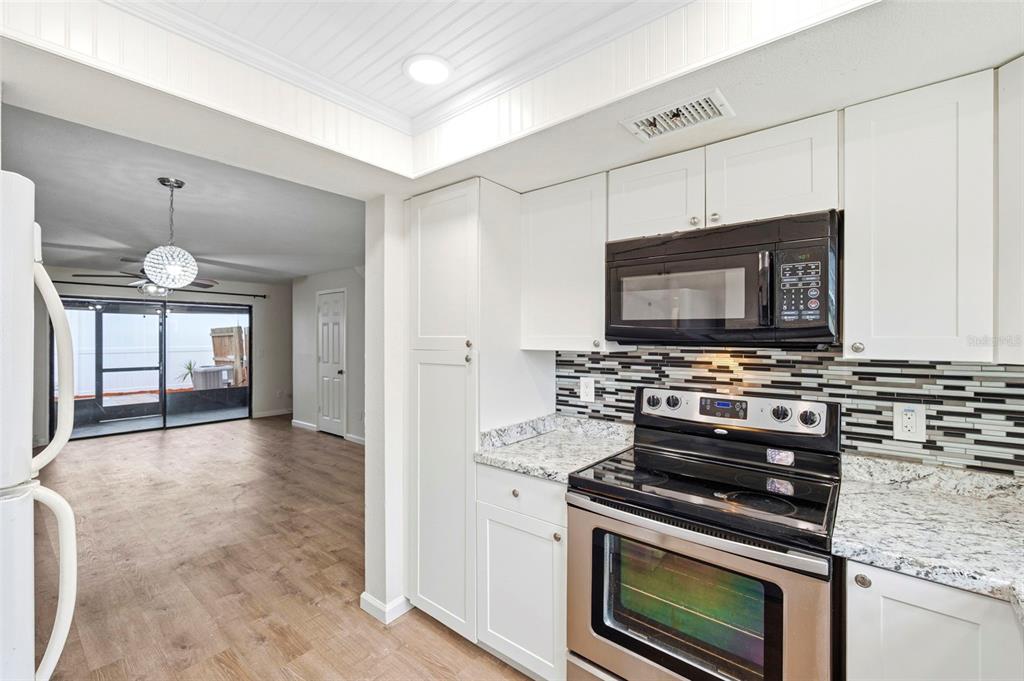 A kitchen with white cabinets, granite countertops, and a black stove overlooks a living area — 2871 S PINES DRIVE UNIT 31, LARGO, FL