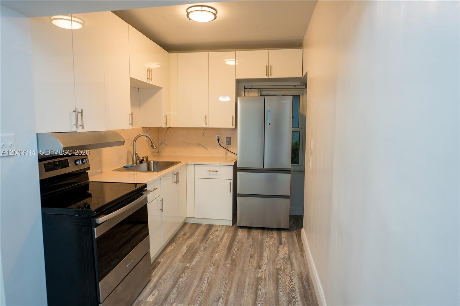 A galley kitchen features white cabinets, stainless steel appliances, and wood-look flooring — 259 NE 56th St, Miami FL 33137, MIAMI, FL