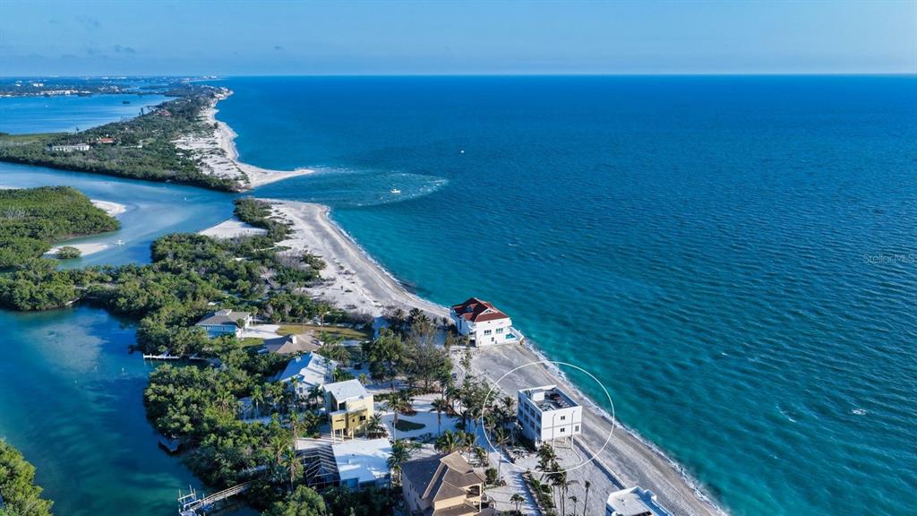An aerial view shows a white multi-story house on a sandy beach near water — 9200 BLIND PASS ROAD, SARASOTA, FL