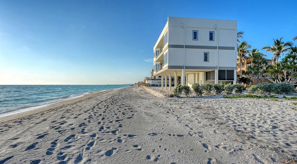 A multi-story white house on stilts sits directly on a sandy beach by the ocean — 9200 BLIND PASS ROAD, SARASOTA, FL
