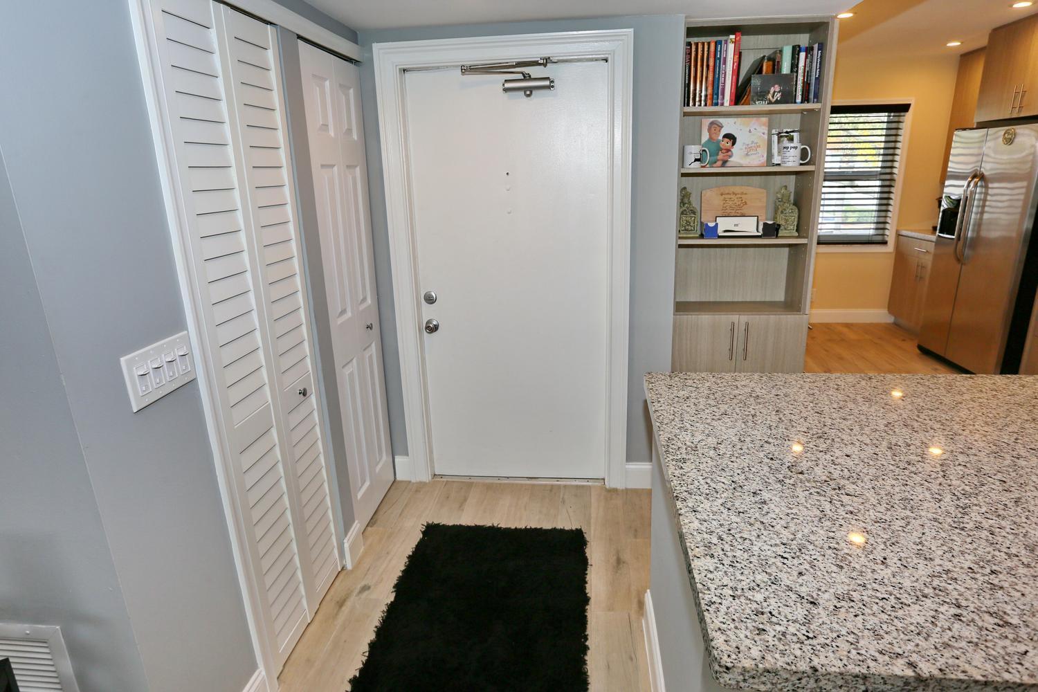 An entryway features a white door, louvered closet doors, a bookshelf, and a granite-topped island — 6550 S Oriole Boulevard # 2050, Delray Beach FL 33446, DELRAY BEACH, FL