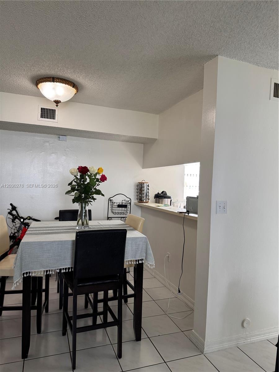 A dining area features a table with a striped cloth, chairs, and a kitchen pass-through — 18250 Mediterranean Blvd # 15, Hialeah FL 33015, HIALEAH, FL