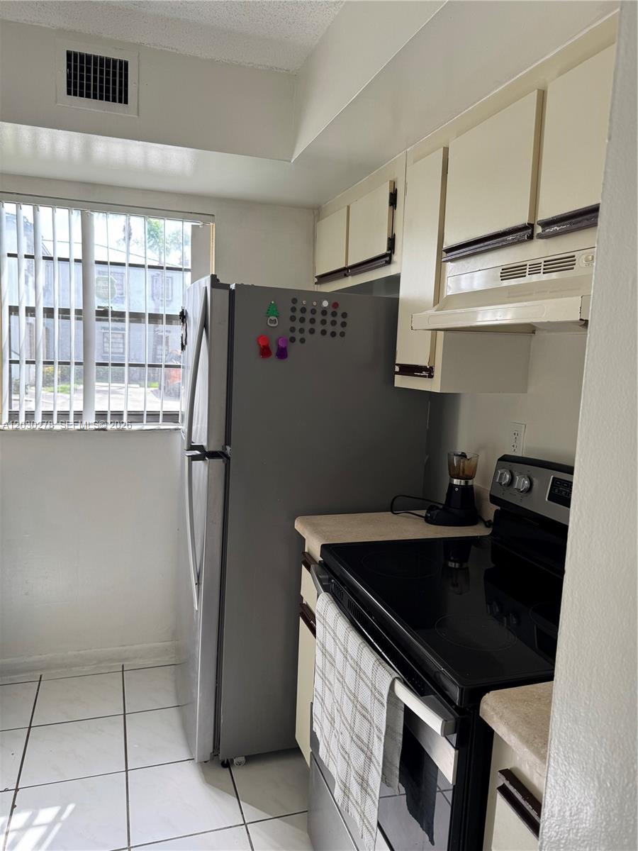 A kitchen features white tile floors, a stainless steel refrigerator, and off-white cabinets — 18250 Mediterranean Blvd # 15, Hialeah FL 33015, HIALEAH, FL