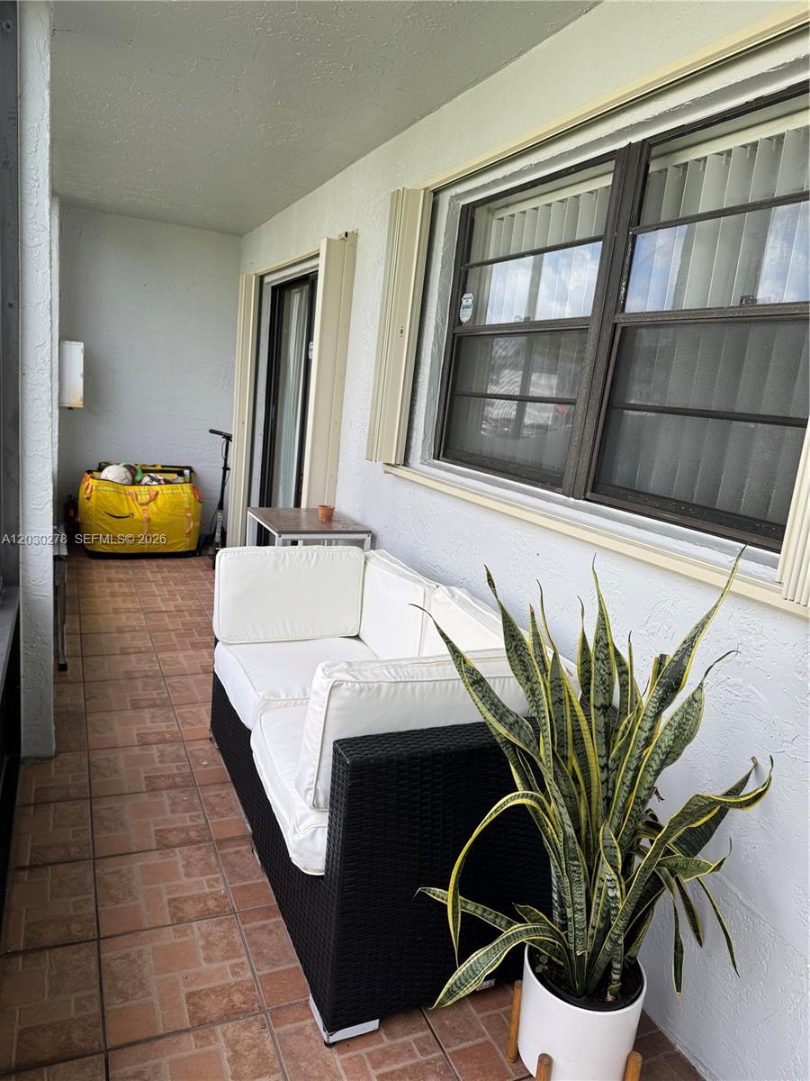 A covered patio features tiled flooring, a black wicker sofa, and a potted snake plant — 18250 Mediterranean Blvd # 15, Hialeah FL 33015, HIALEAH, FL