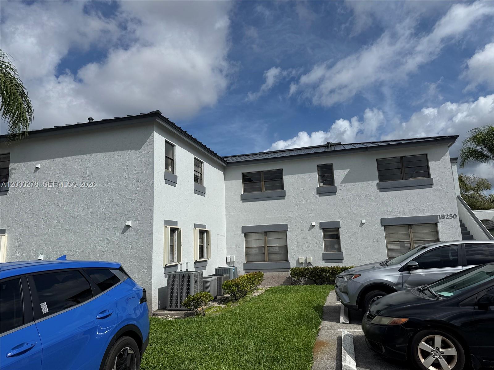 A two-story white stucco apartment building features a metal roof and parked cars outside — 18250 Mediterranean Blvd # 15, Hialeah FL 33015, HIALEAH, FL