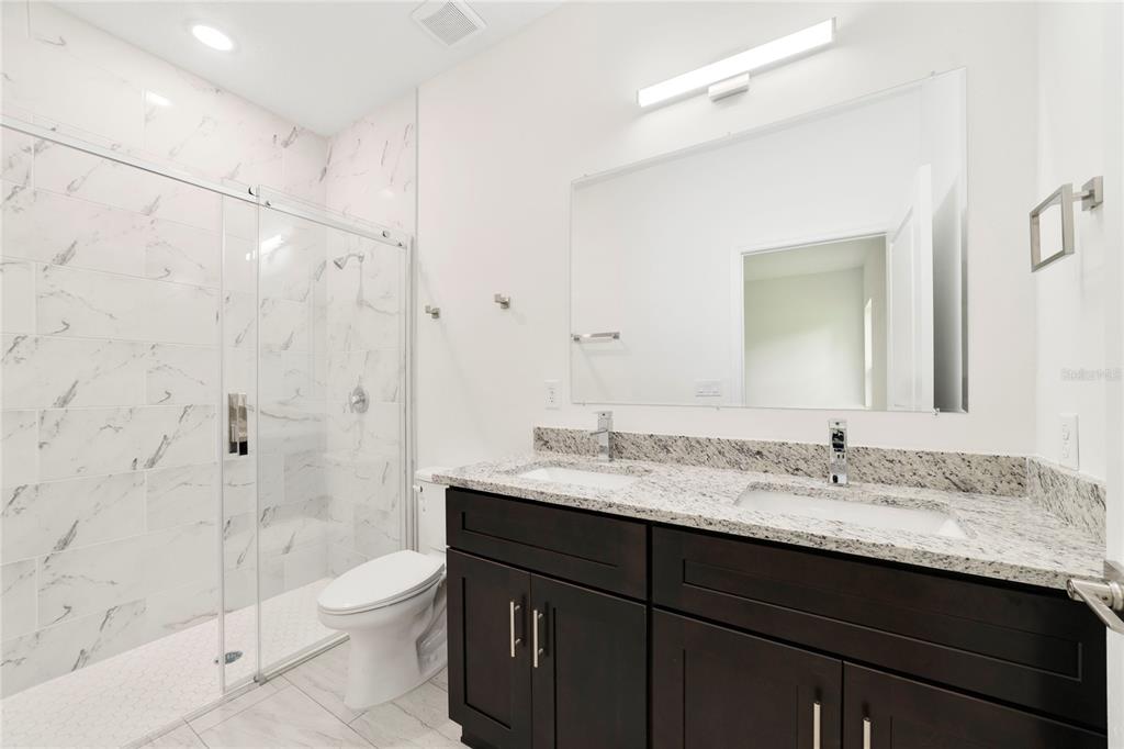 A bathroom features a double vanity with granite countertops, dark cabinets, and a glass-enclosed shower — 3355 W MARIE DRIVE, CITRUS SPRINGS, FL