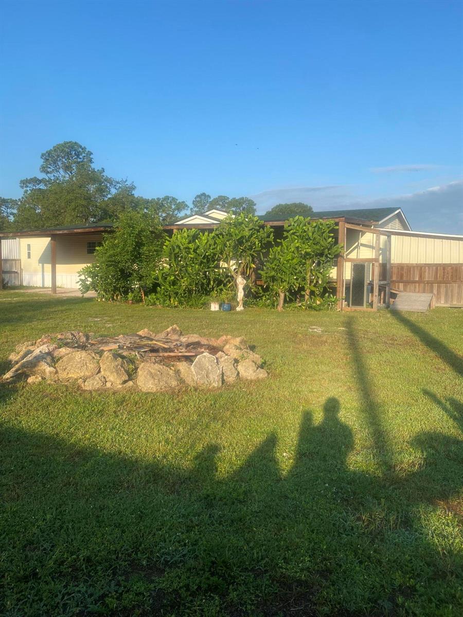 A grassy backyard features a stone fire pit and a mobile home with a covered porch — 170 S Lindero Street, Clewiston FL 33440, CLEWISTON, FL