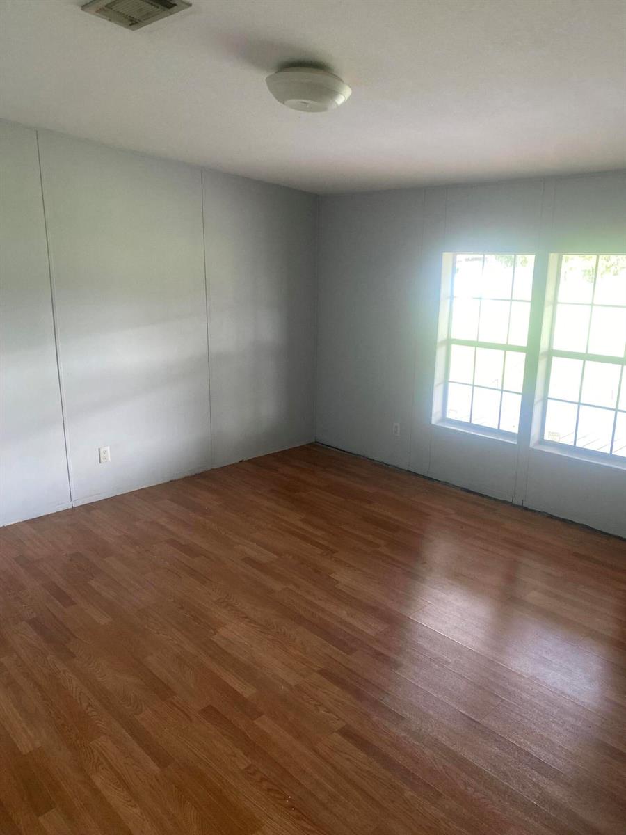 An empty room features light gray paneled walls, wood-look flooring, and two windows — 170 S Lindero Street, Clewiston FL 33440, CLEWISTON, FL