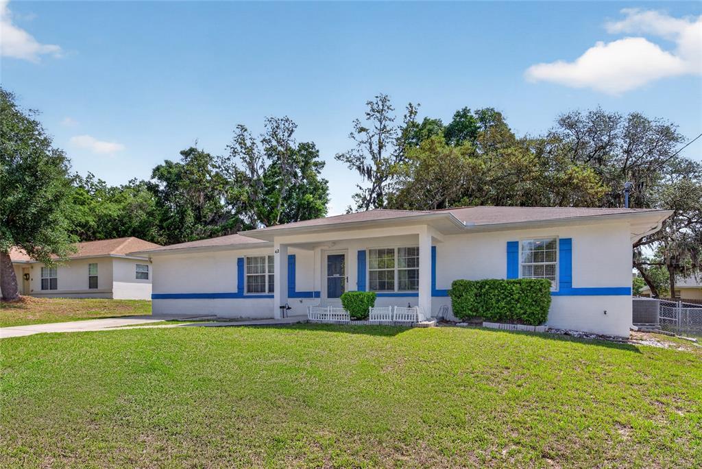 A single-story white house with blue trim and a front porch sits on a lawn — 42 LARCH RADIAL, OCALA, FL
