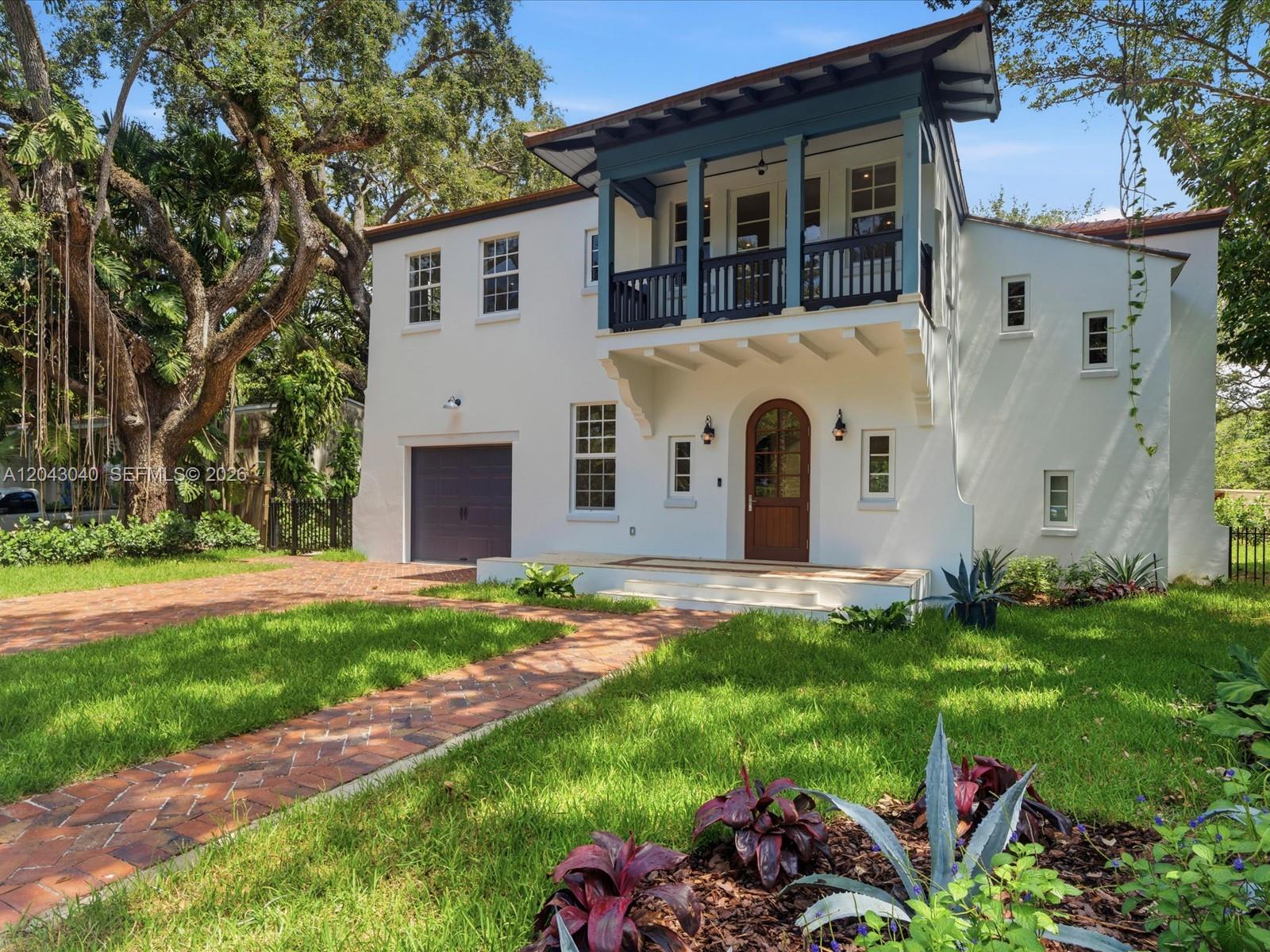 A two-story white stucco house features a blue-trimmed balcony, arched front door, and brick driveway — 6333 SW 69th St, South Miami FL 33143, SOUTH MIAMI, FL