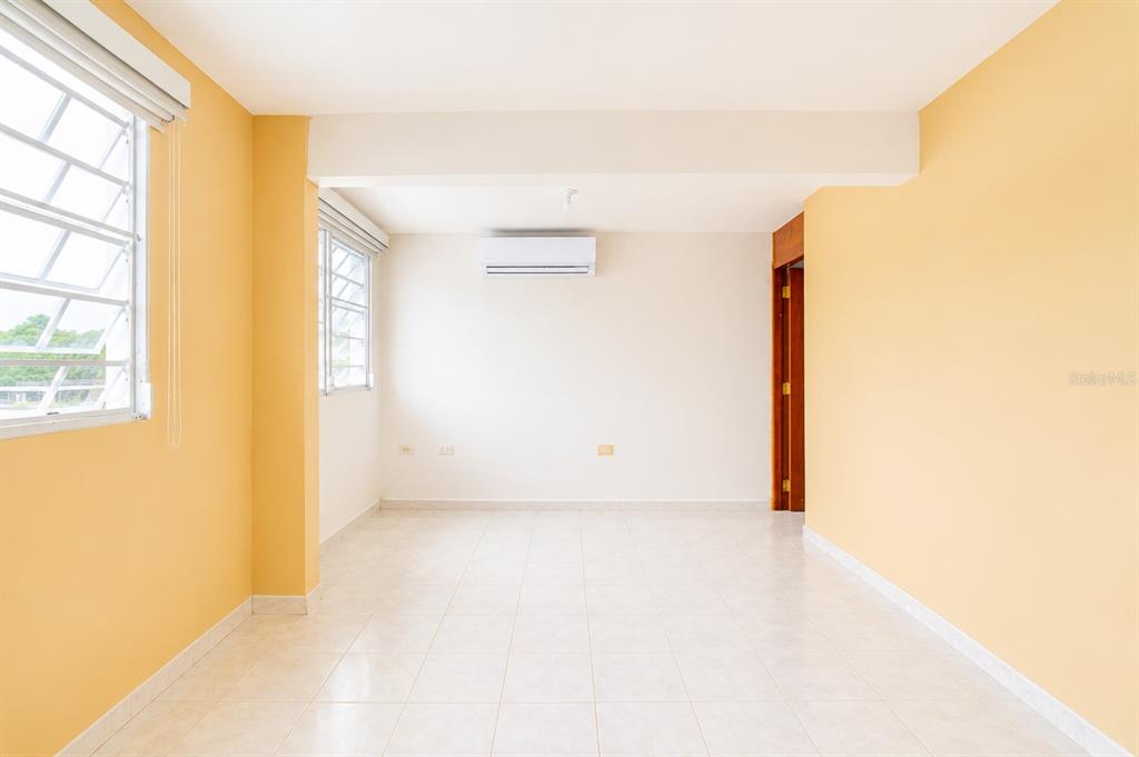 An empty room with yellow walls, white tile floors, two windows, and a wall-mounted air conditioner — Calle C URB LOS CHOFERES CALLE C UNIT 28, SAN JUAN, PR