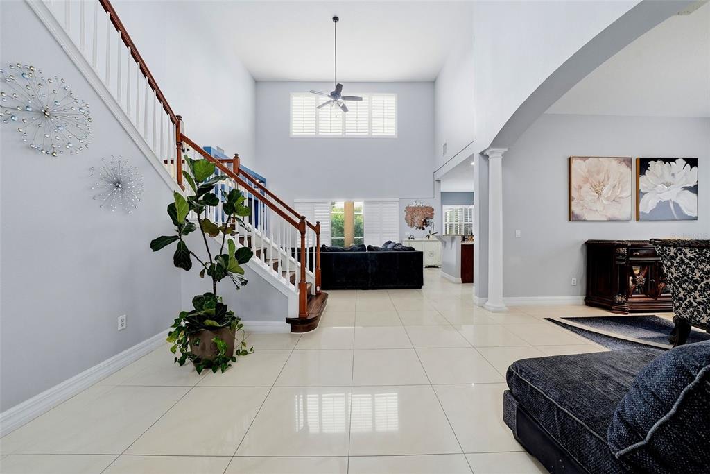 A spacious living room features high ceilings, a staircase, tile flooring, and a ceiling fan — 18043 COZUMEL ISLE DRIVE, TAMPA, FL