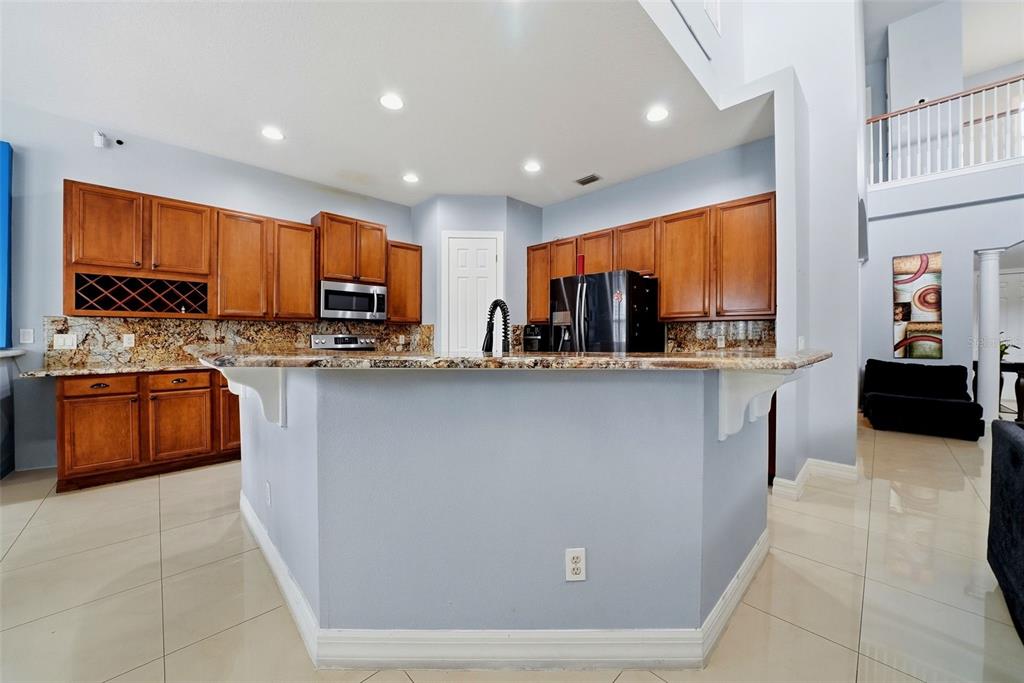 A kitchen features wood cabinets, granite countertops, a central island, and light-colored tile flooring — 18043 COZUMEL ISLE DRIVE, TAMPA, FL