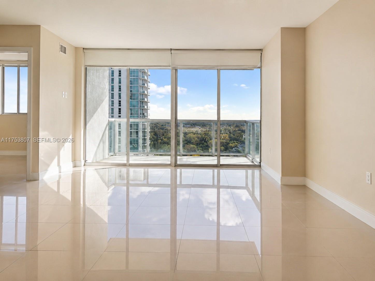 An empty room features glossy tile floors, beige walls, and large sliding glass balcony doors — 1861 NW S River Dr # 1504, Miami FL 33125, MIAMI, FL