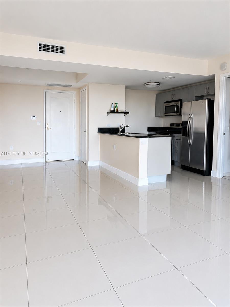 An open-concept kitchen with stainless steel appliances and a breakfast bar overlooks a tiled living area — 1861 NW S River Dr # 1504, Miami FL 33125, MIAMI, FL