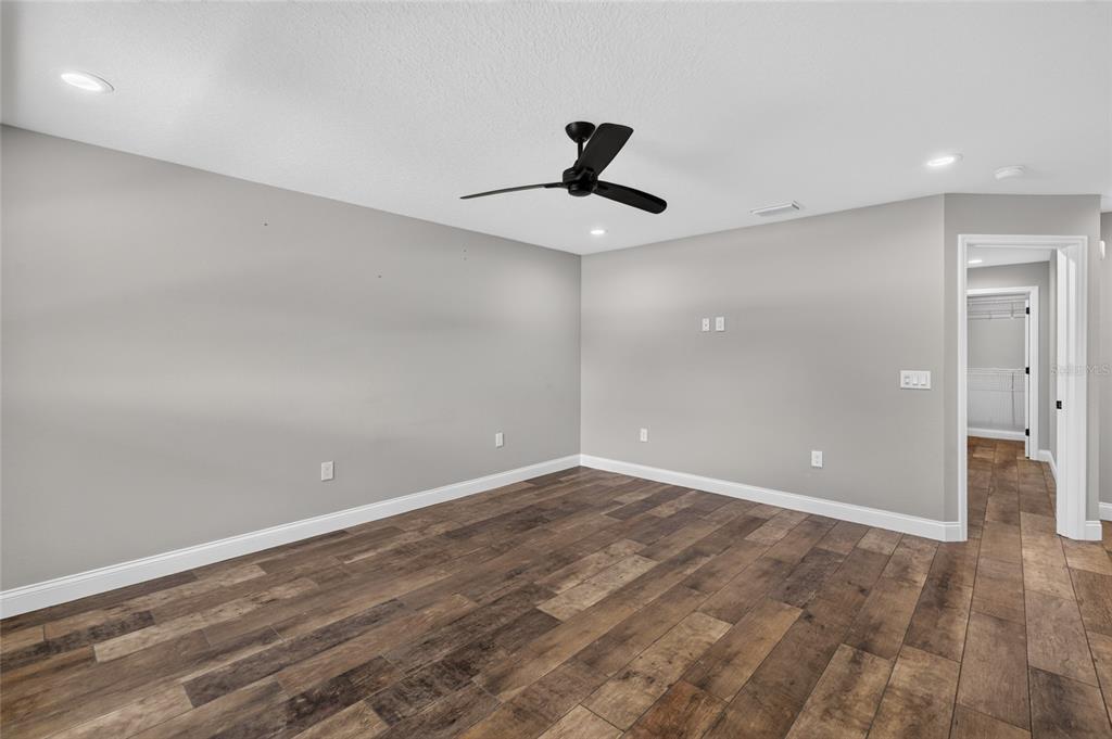 An empty room features gray walls, wood-look tile flooring, a ceiling fan, and a walk-in closet — 6631 THORNHILL ROAD, WINTER HAVEN, FL
