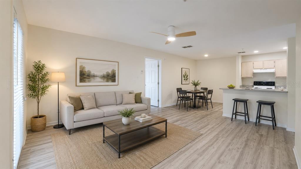 A living room and kitchen area with light wood-look flooring and neutral walls — 7428 VISTA WAY UNIT 104, BRADENTON, FL