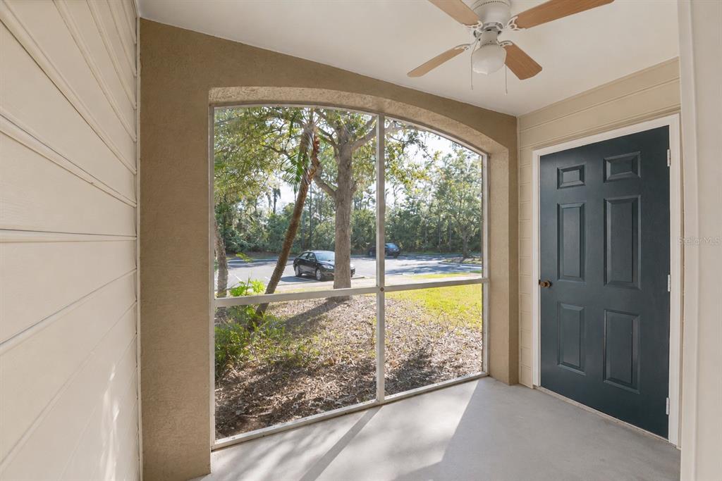 A screened-in porch with a ceiling fan, concrete floor, and a dark blue entry door — 7428 VISTA WAY UNIT 104, BRADENTON, FL