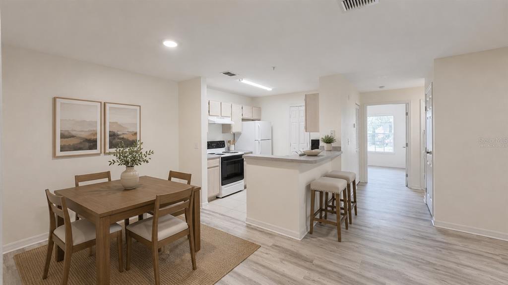 A dining area with a table and chairs sits adjacent to a kitchen with white appliances — 7428 VISTA WAY UNIT 104, BRADENTON, FL