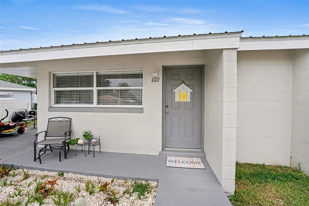 The exterior of a single-story home features a gray front door and a concrete porch — 45 QUEENS COURT, FROSTPROOF, FL