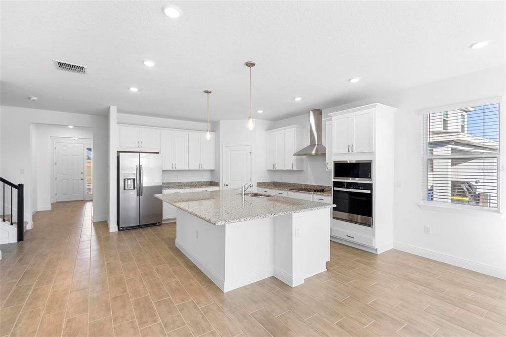 A modern kitchen features white cabinets, granite countertops, a central island, and stainless steel appliances — 2028 KEYSTONE PASS BOULEVARD, MINNEOLA, FL